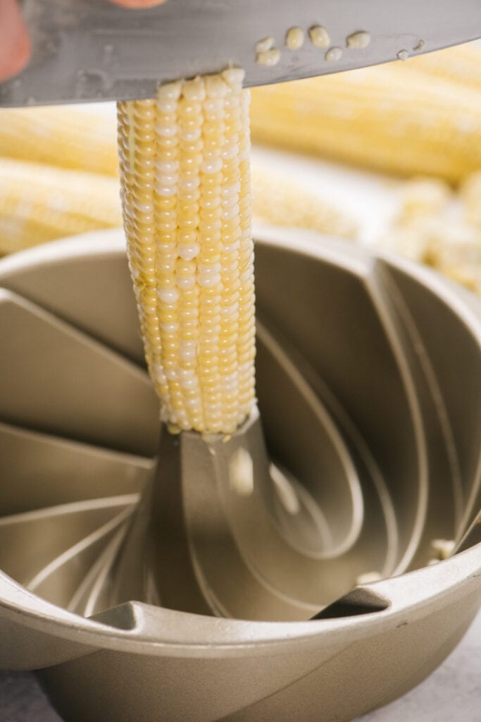 Running a chef's knife along an ear of corn standing upright in a bundt pan to slice off the kernels.