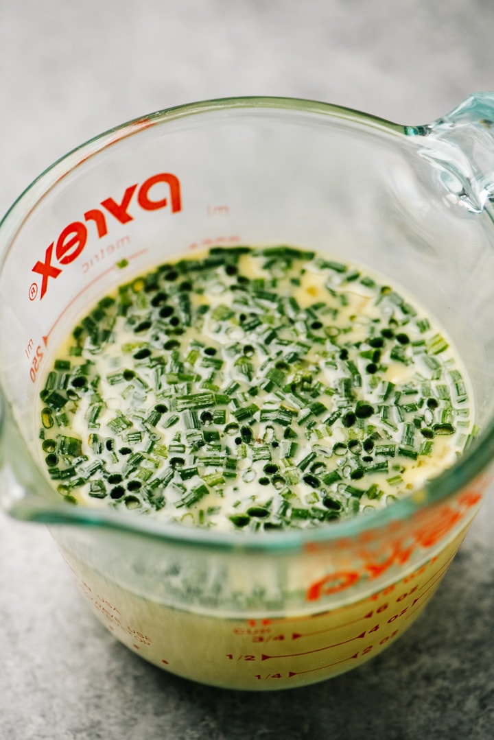 Milk, honey, eggs, and chives whisked in a glass measuring cup.