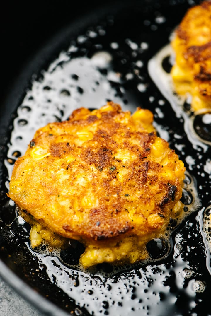 Side view, golden brown corn fritters in a cast iron skillet.
