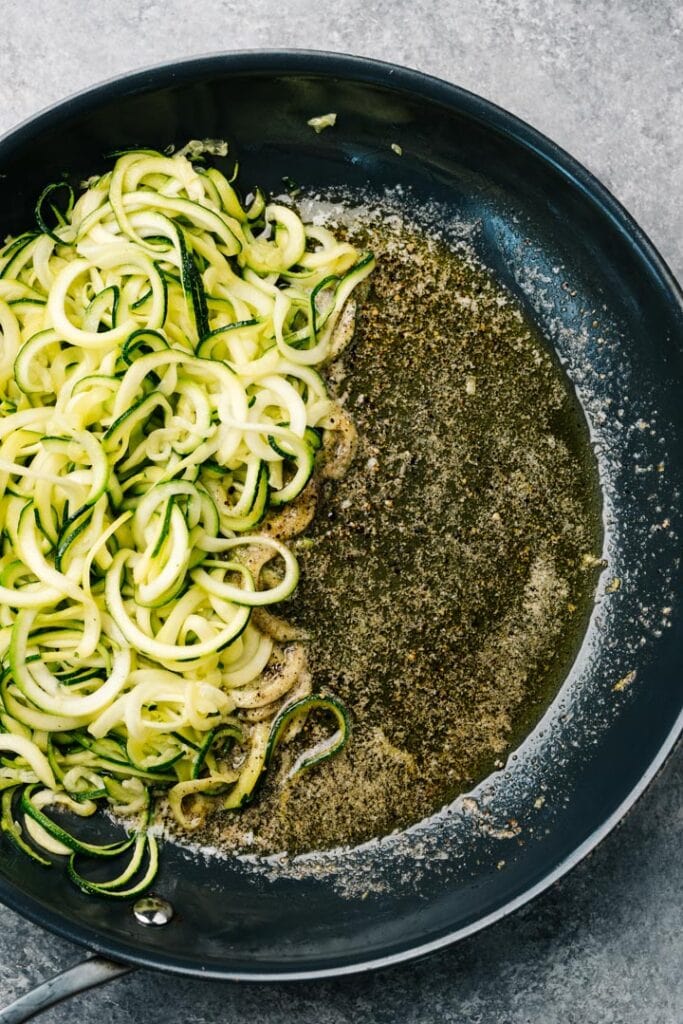 Melted butter with ground pepper in a skillet, with zucchini noodles to the side.