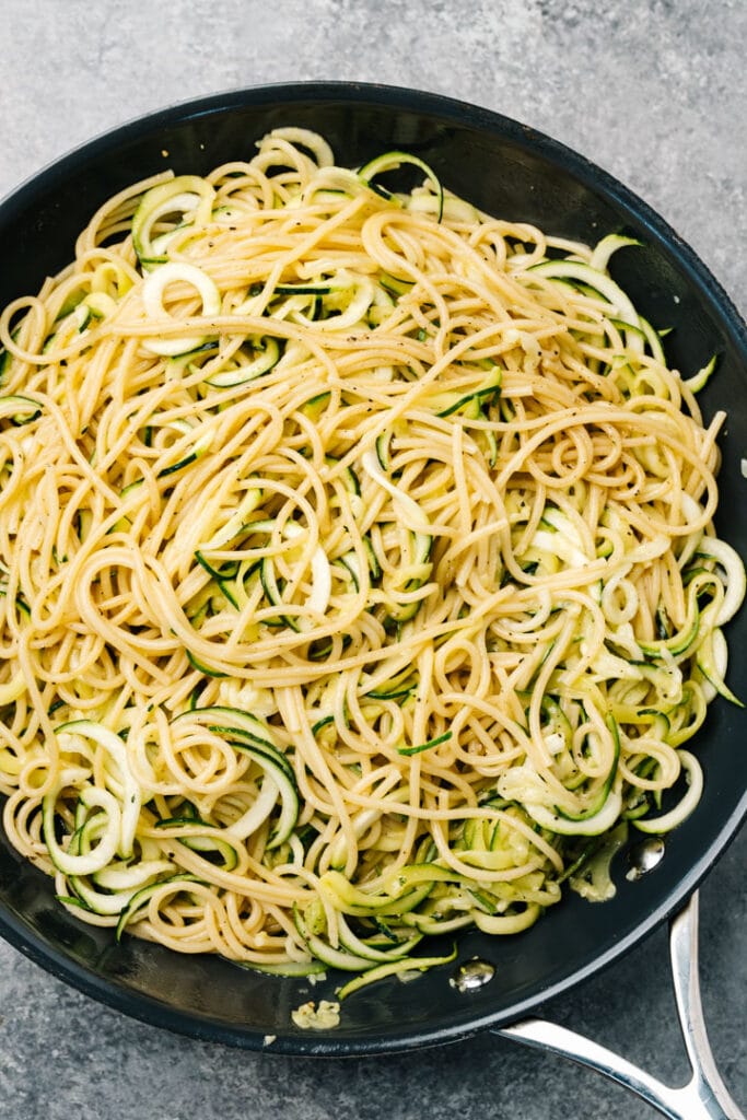 Sautéed zucchini tossed with spaghetti and butter in a skillet.
