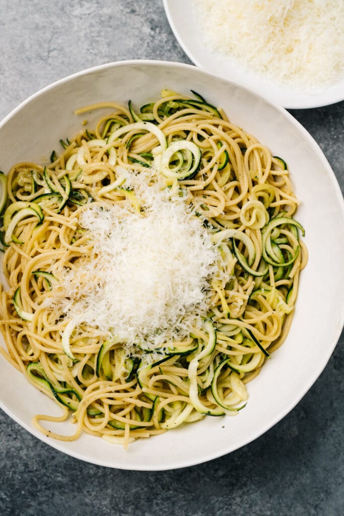 Adding parmesan cheese to a bowl of zucchini and pasta.