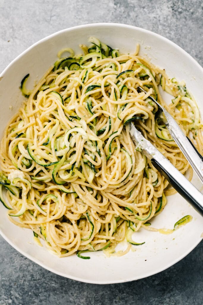 Zucchini pasta in a large white bowl with tongs.
