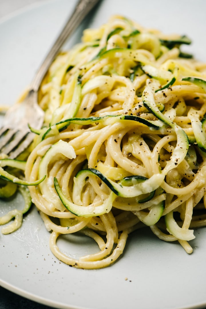 Side view, creamy zucchini pasta on a blue plate with a vintage silver fork.