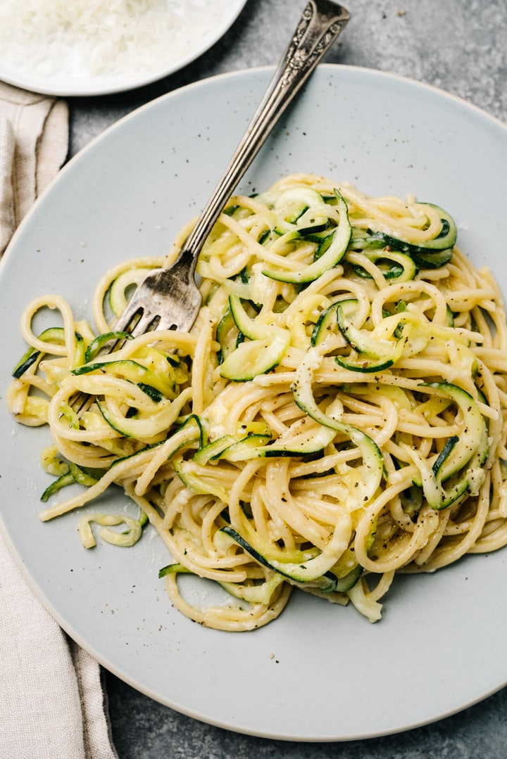 Zucchini noodles and spaghetti tossed in a creamy parmesan sauce on a blue plate with a linen napkin to the side.