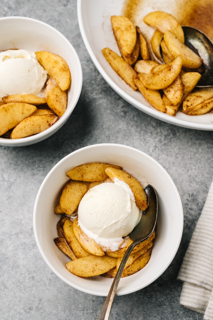 Two bowls of air fryer apples topped with ice cream on a cement background.
