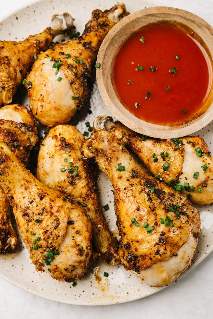 Air fryer drumsticks on a speckled tan plate with a small bowl of hot sauce for dipping.
