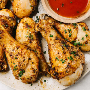 Crispy chicken drumsticks made in the air fryer on a platter with a small bowl of hot sauce.