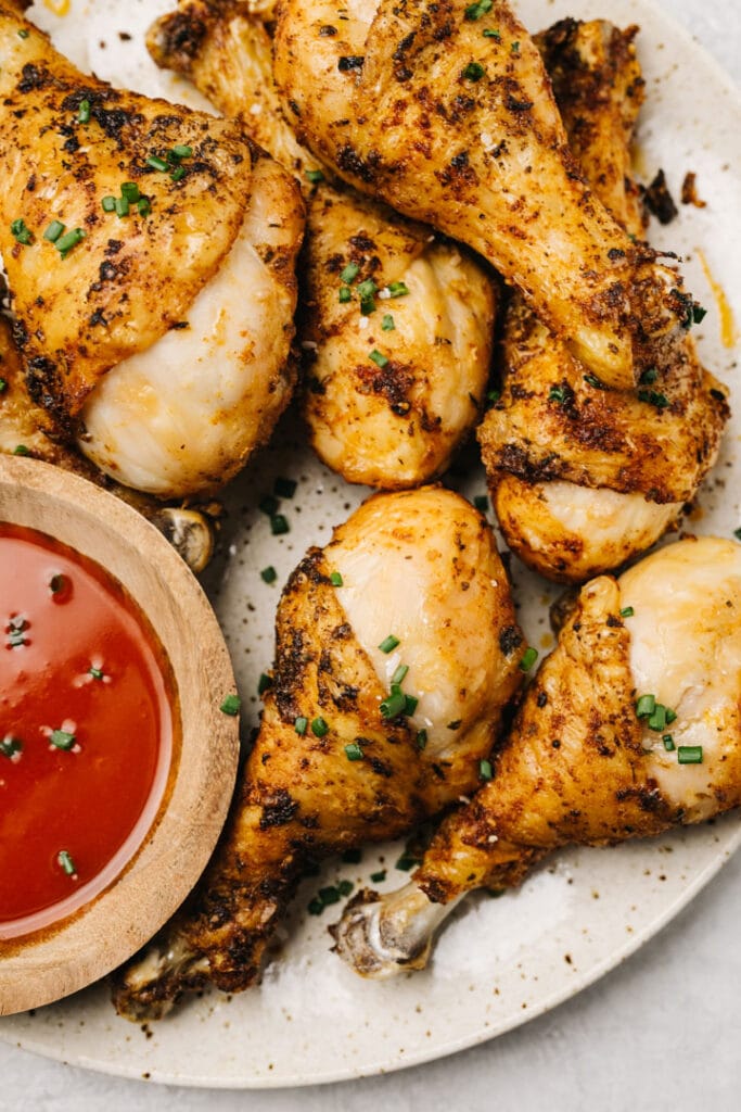 Air fryer chicken drumsticks on a tan speckled plate with hot sauce on the side.