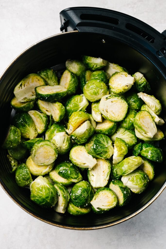 Raw seasoned brussels sprouts in the basket of an air fryer.