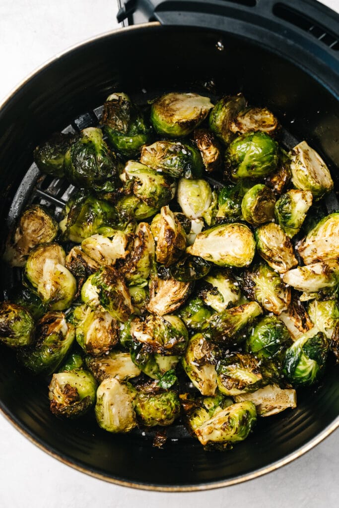 Crispy roasted air fried brussels sprouts in the basket of an air fryer.