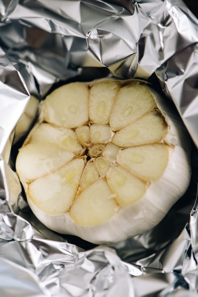 A whole head of garlic with the top sliced off nestled in a piece of foil.