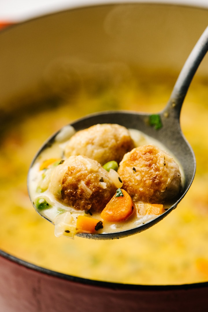 Creamy chicken meatball soup in a metal ladle, hovering over a red dutch oven.