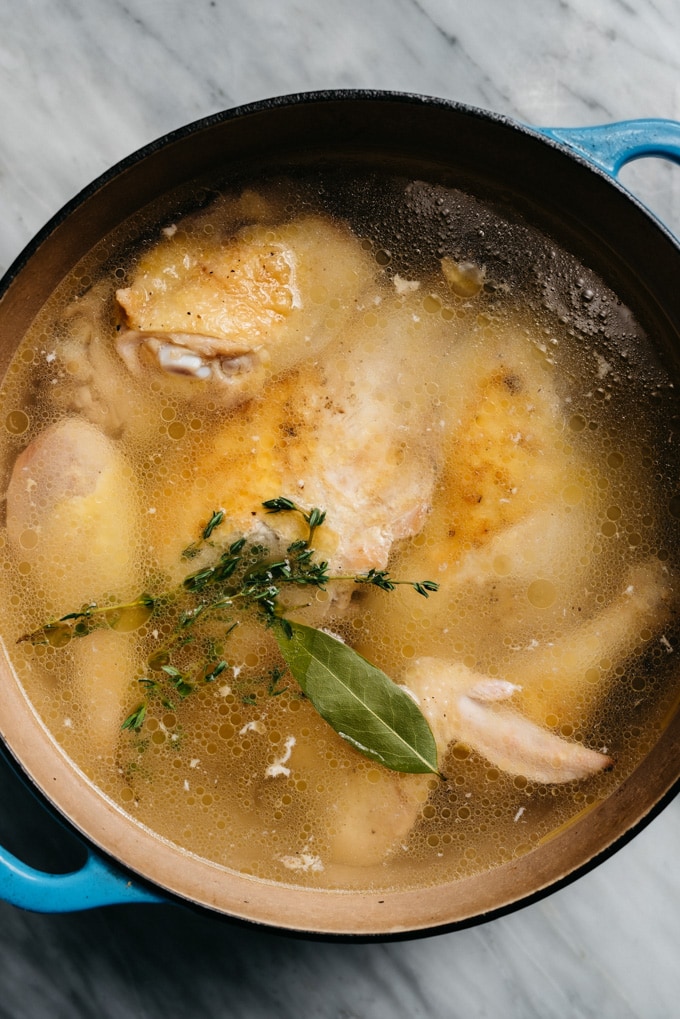 A whole chicken cut into pieces simmering with fresh herbs to make homemade soup.