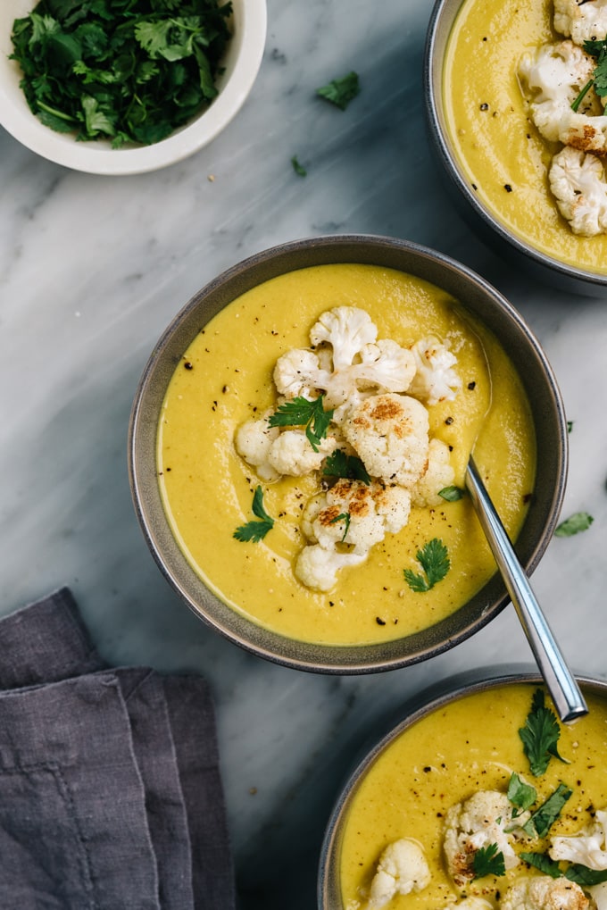 Three bowls of healthy curried cauliflower soup on a marble background with a grey linen napkin.