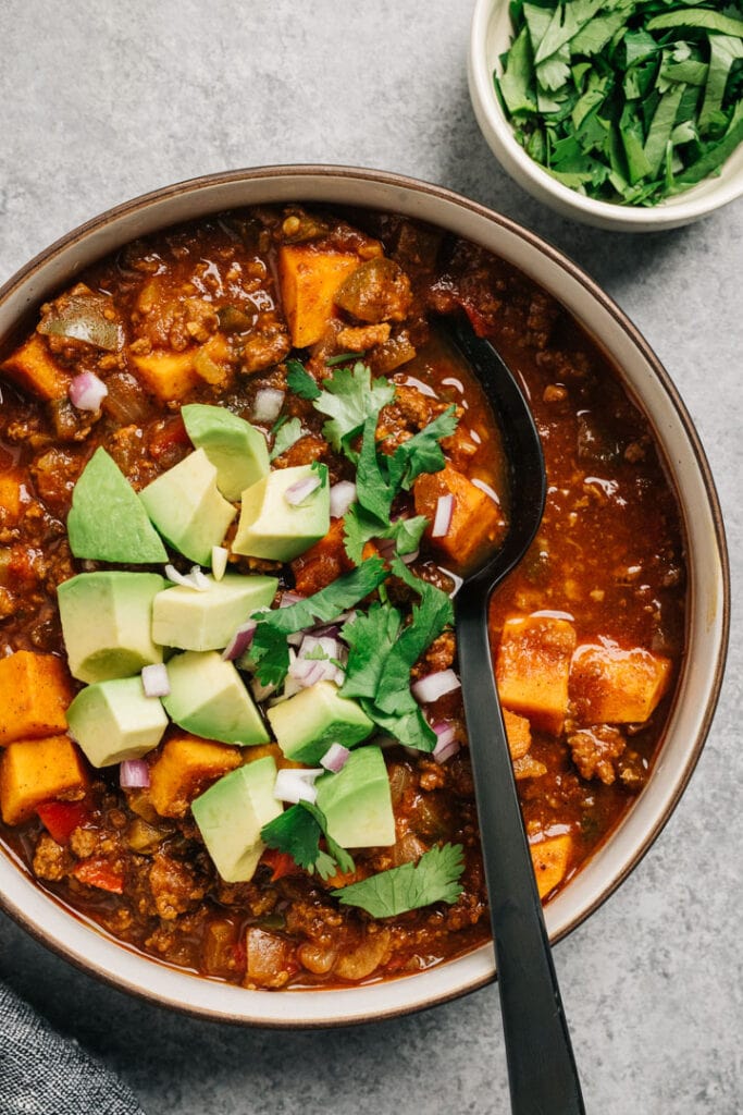 A bowl of Whole30 and paleo sweet potato and ground beef chili garnished with avocado and cilantro.