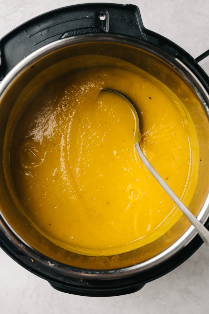 A ladled tucked into pureed butternut squash soup in an instant pot.