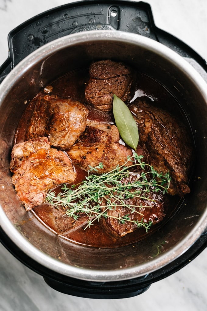 Seared pieces of chuck roast with beef broth and seasonings topped with fresh herbs in an instant pot.