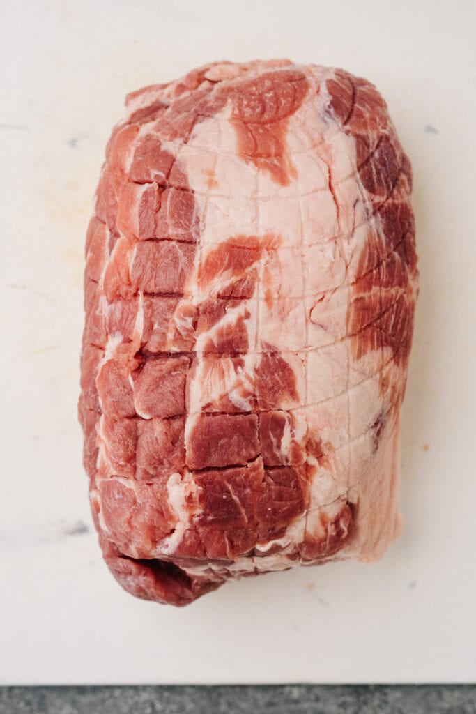 Boneless pork butt on a white cutting board showing marbling.