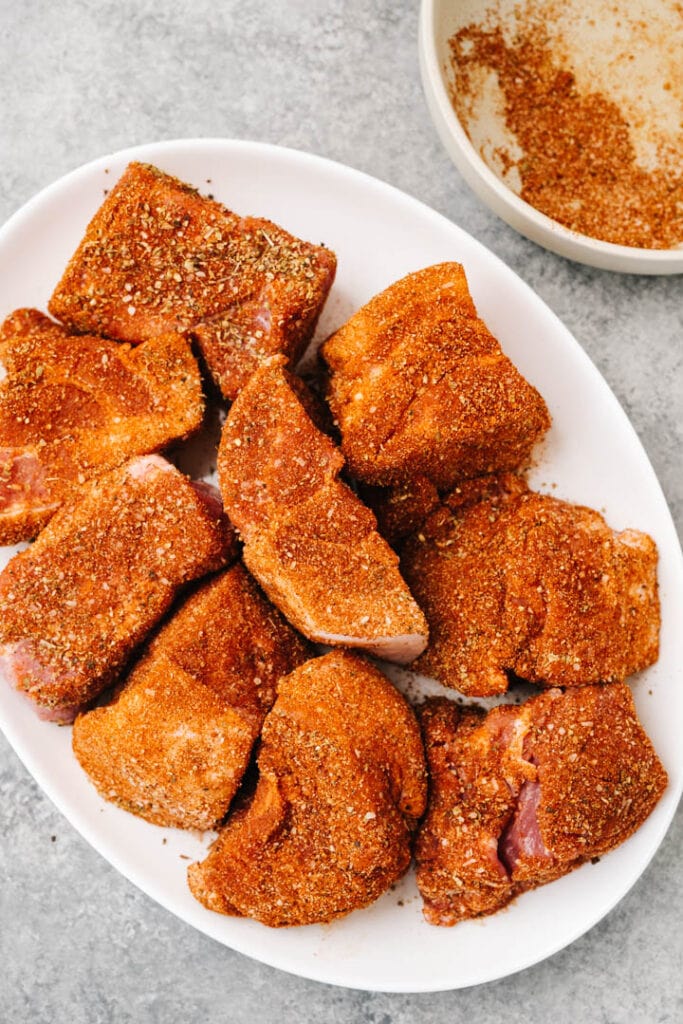 Pork pieces coated in dry rub on a white platter.