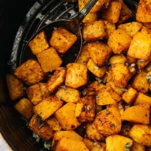 Crispy roasted butternut squash cubes in the basket of an air fryer with a silver vintage serving spoon.