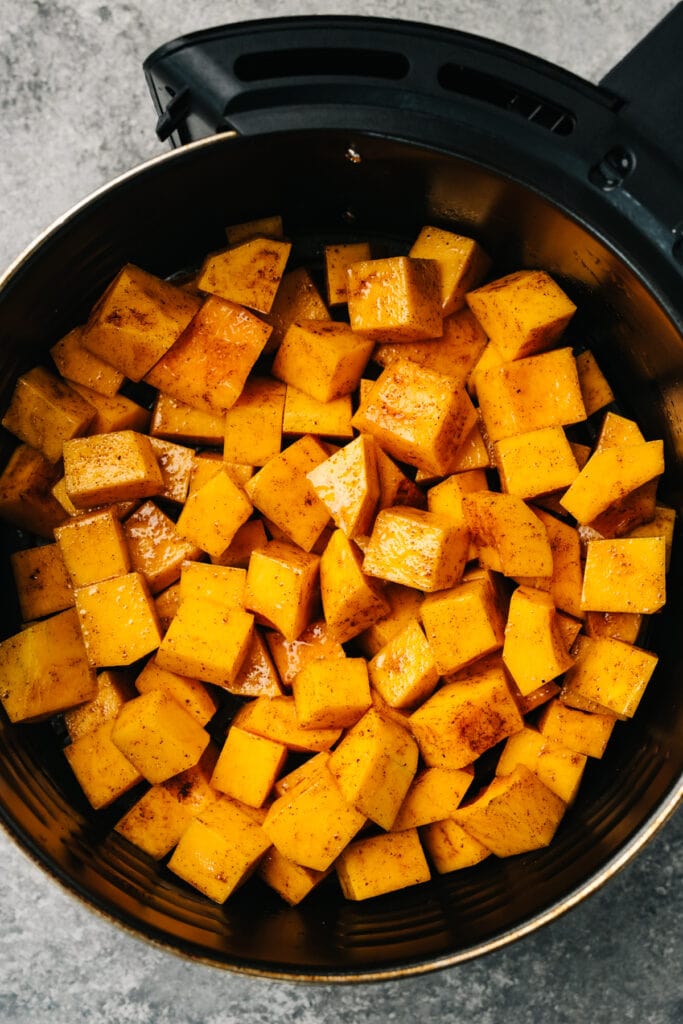 Diced and seasoned butternut squash in an even layer in the basket of an air fryer.