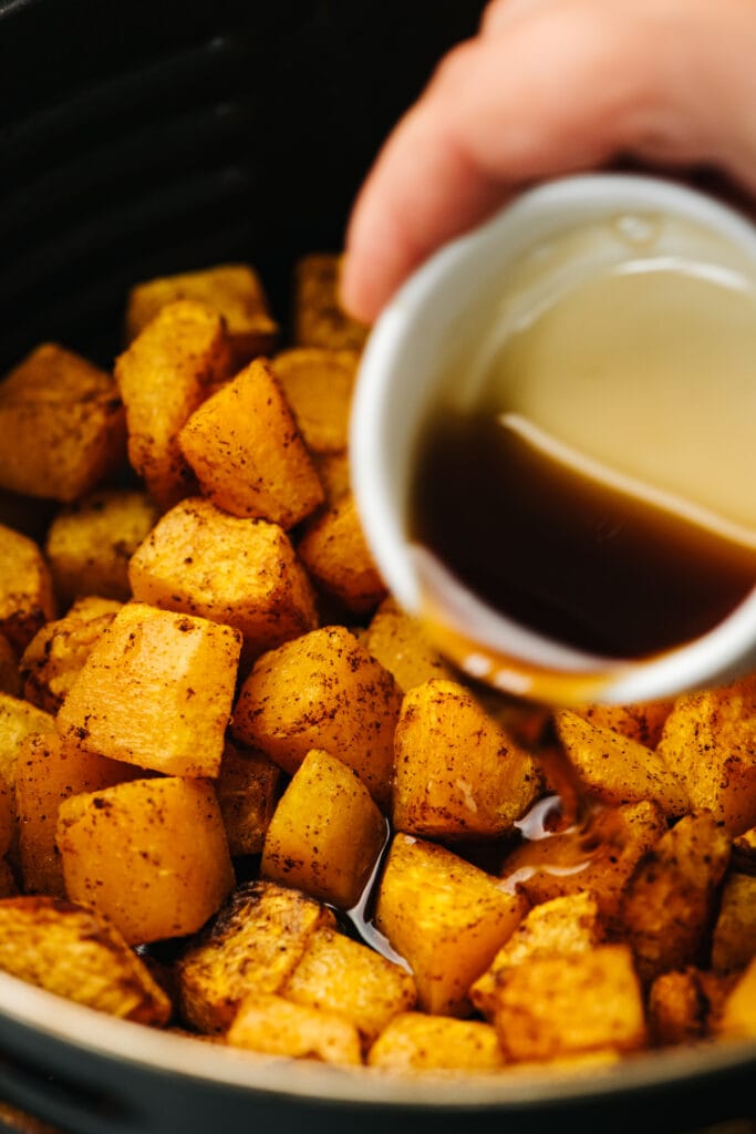 Drizzling maple syrup over air fryer butternut squash cubes.