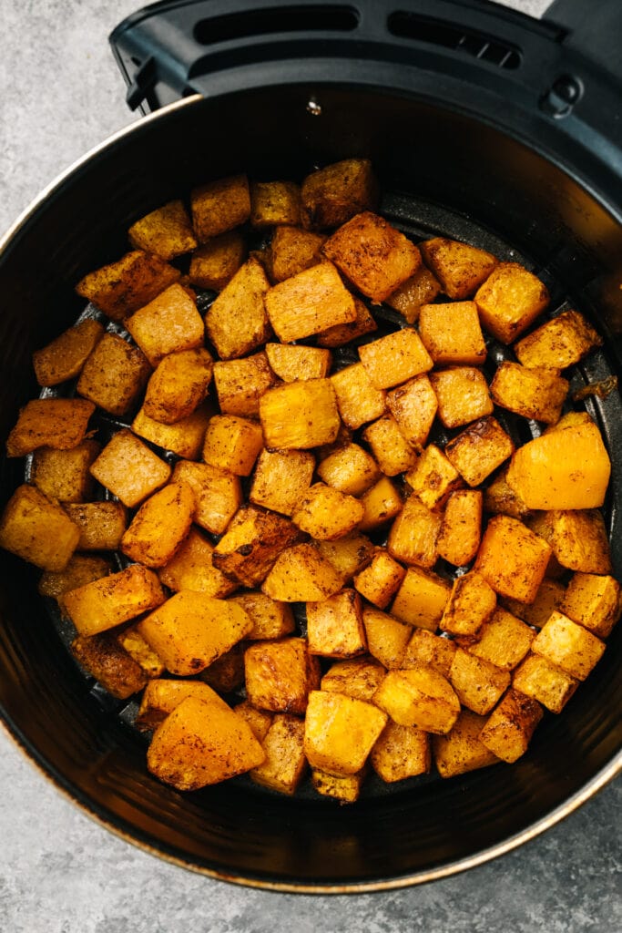 Maple sweetened butternut squash cubes in the basket of an air fryer.