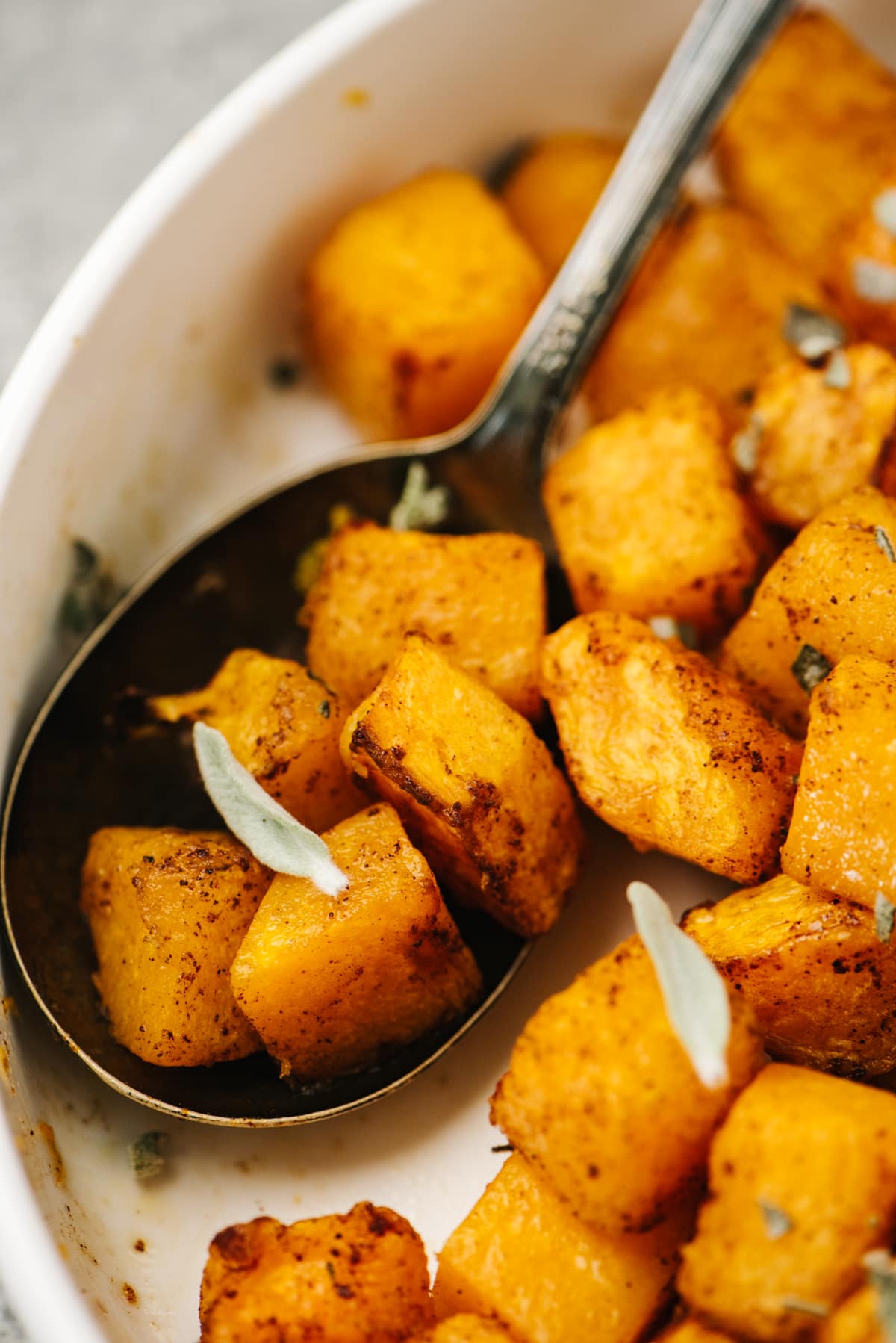 Air fryer butternut squash cubes resting in a vintage serving spoon in a white bowl.