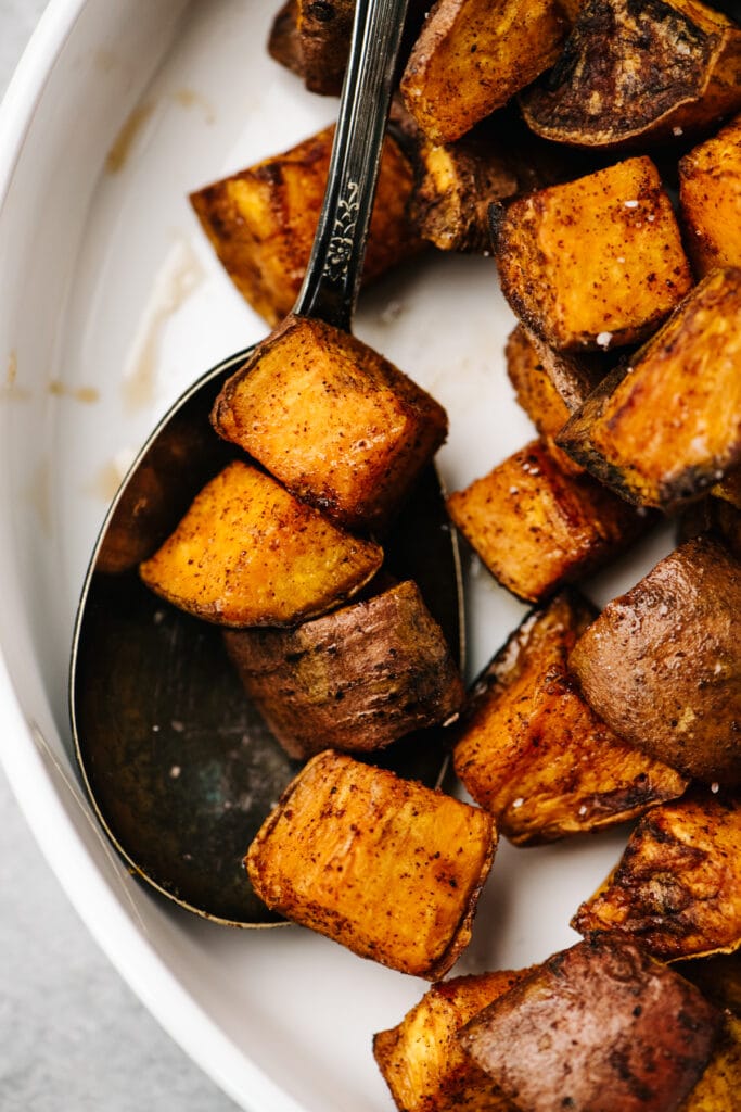 A serving spoon tucked into a bowl of air fryer sweet potato cubes.