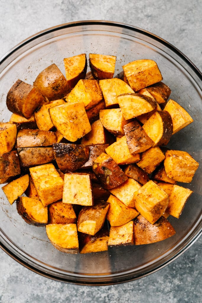 Diced sweet potatoes tossed with olive oil, cinnamon, and salt in a glass mixing bowl.