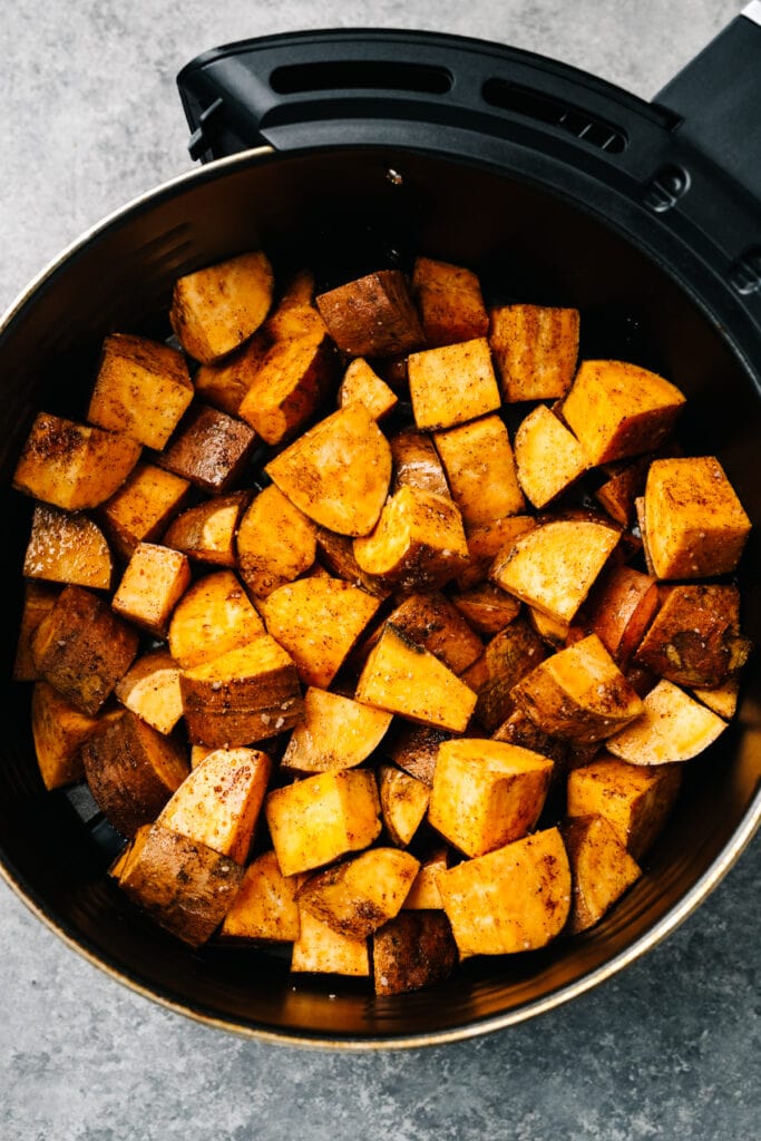Seasoned diced sweet potatoes in an even layer in an air fryer basket.