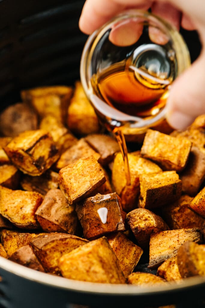 Drizzling maple syrup over air fryer sweet potatoes.