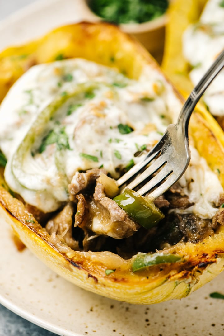 A fork digging into a stuffed spaghetti squash, filled with cheesesteak filling and topped with provolone cheese.