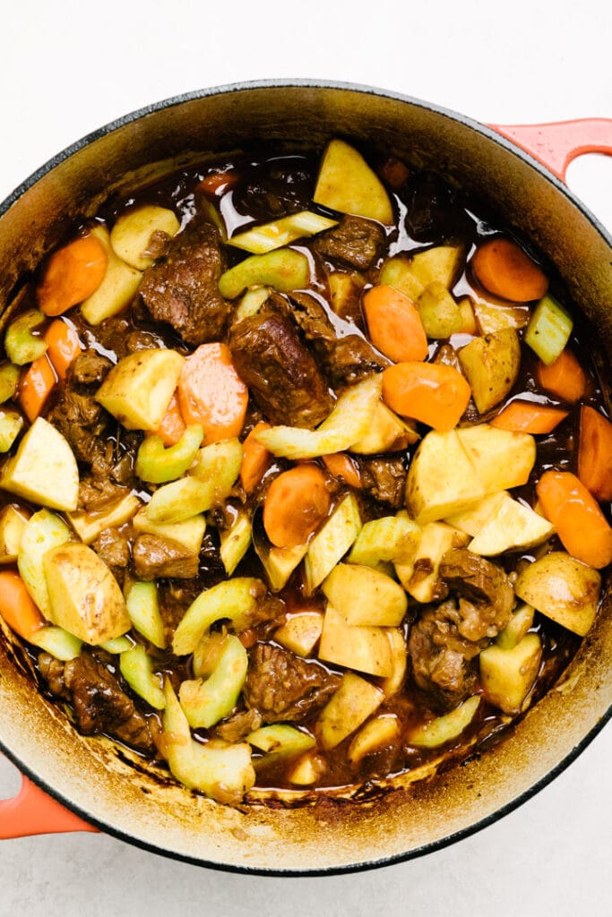 Carrots, celery, and potatoes added to partially cooked beef stew in a dutch oven.