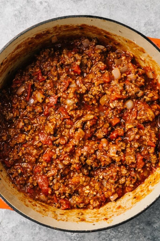 Tomato based ground meat sauce in a red dutch oven.