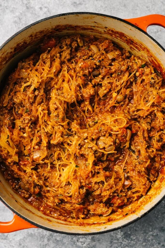 Roasted spaghetti squash strands mixed with tomato ground beef sauce in a red dutch oven.