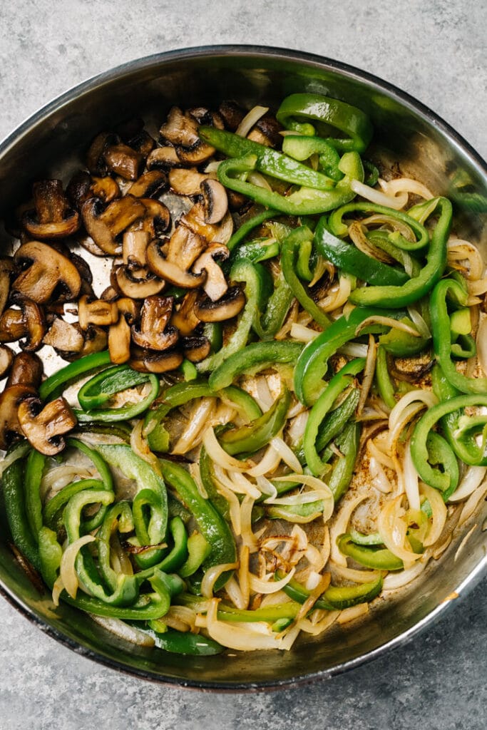 Sauteed green bell peppers, onions, and mushrooms in a skillet.