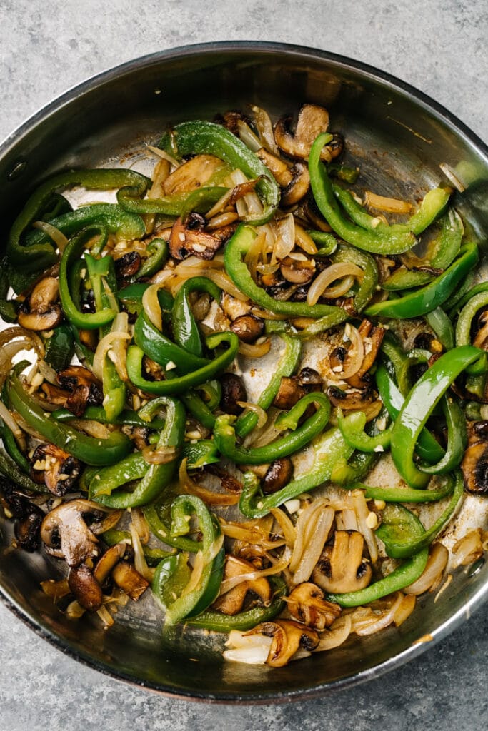 Sauteed green bell peppers, onions, and mushrooms in a skillet with garlic, salt, and pepper.