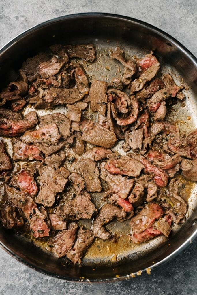 Thin slices of steak searing in a skillet.