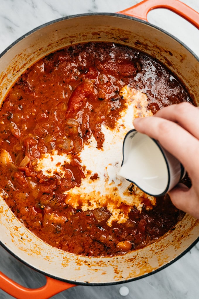 Adding heavy cream to homemade tomato pasta sauce.