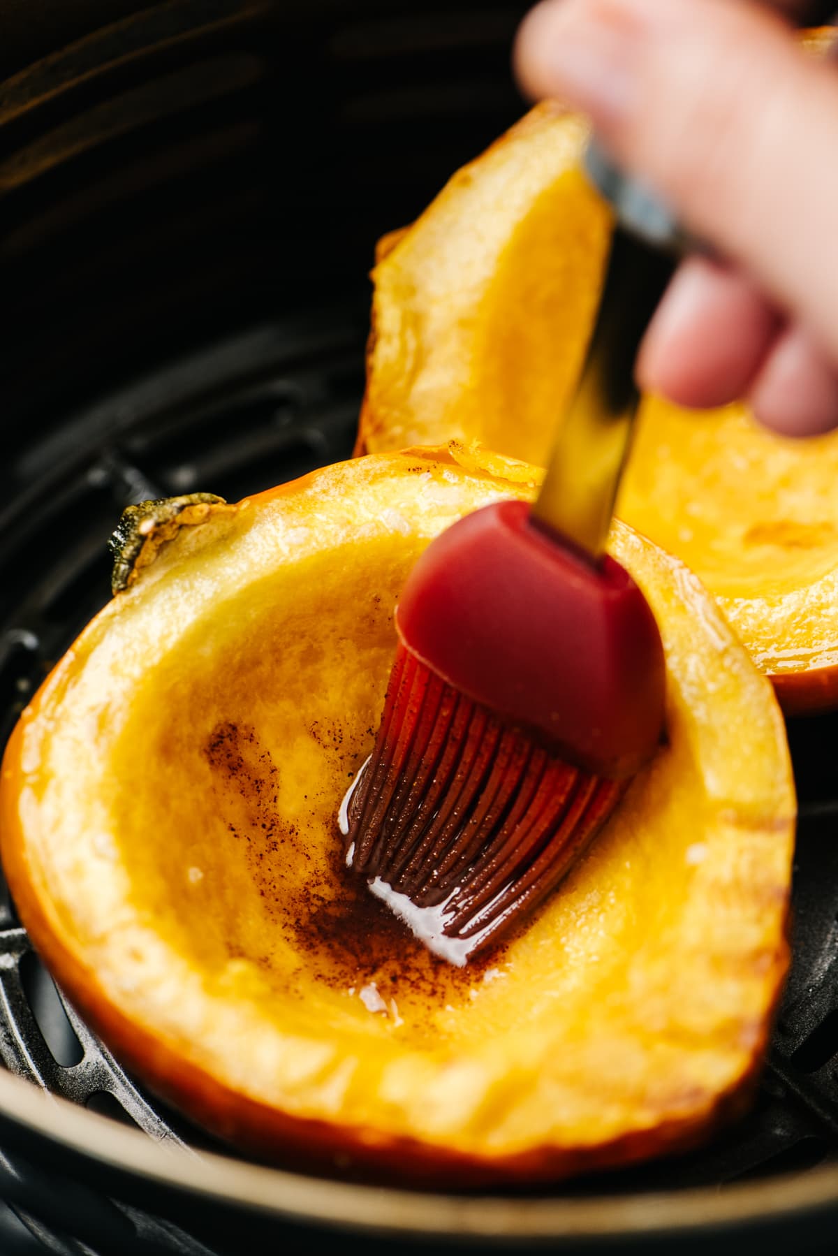 Brushing air fryer acorn squash halves with maple browned butter.