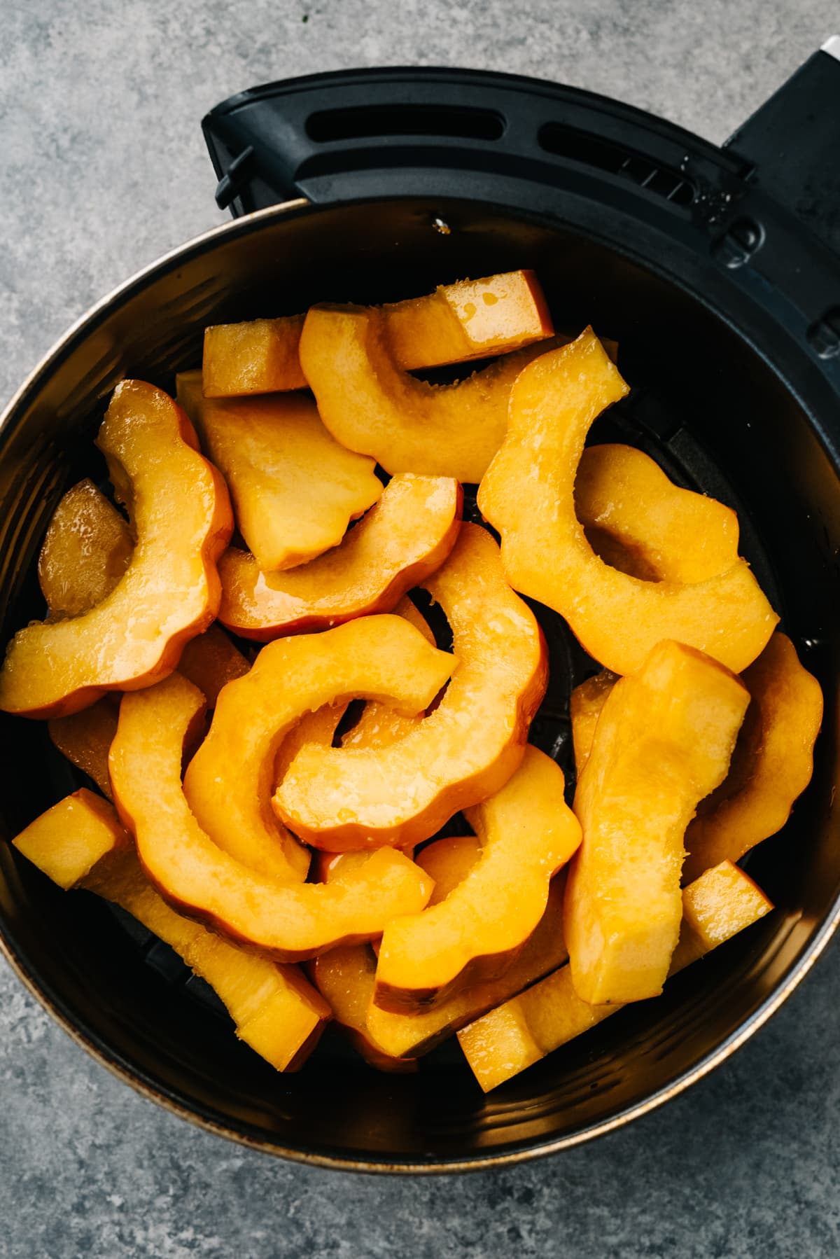 Sliced acorn squash tossed with olive oil and salt in the basket of an air fryer.