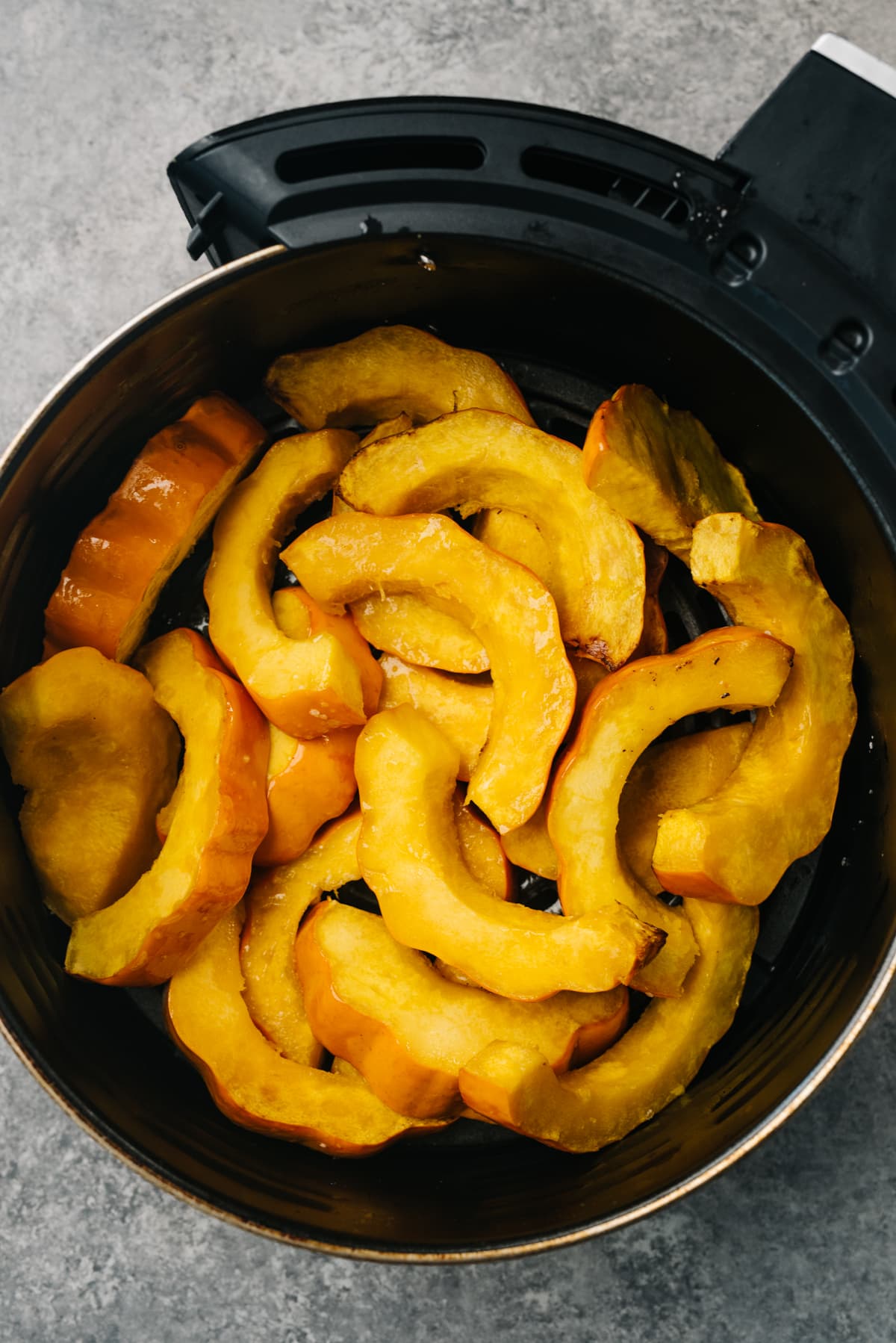 Acorn squash slices in the basket of an air fryer halfway through cooking.
