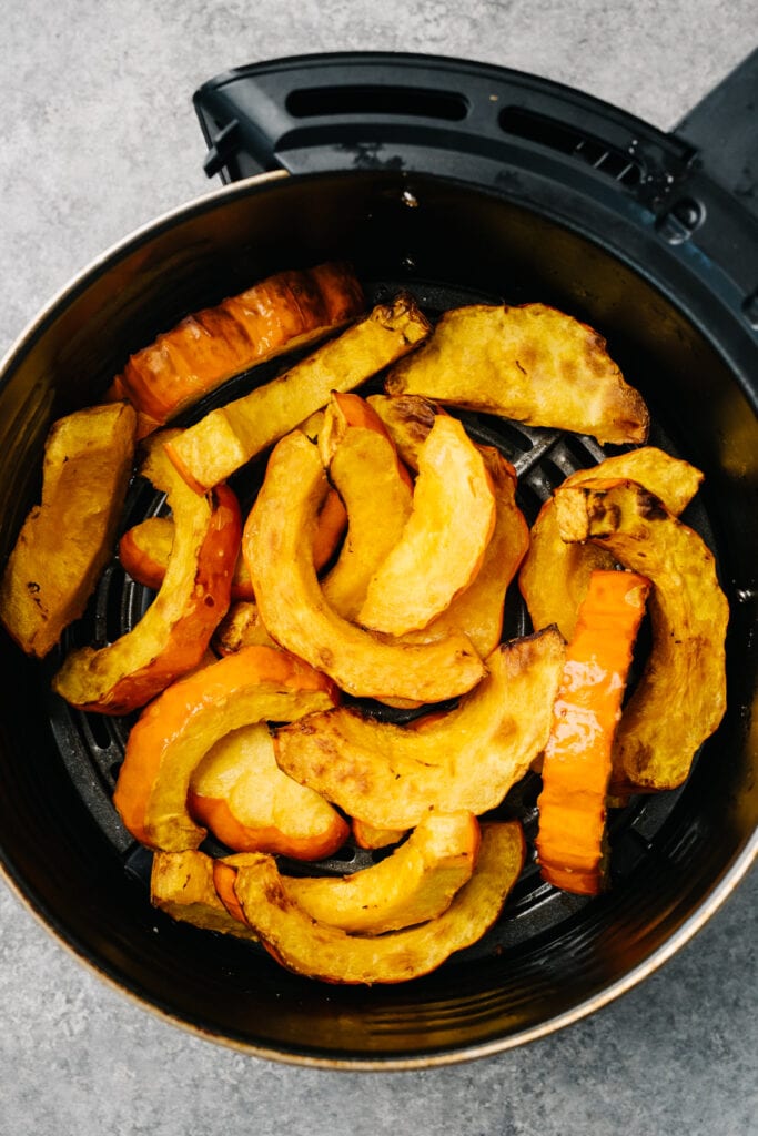 Fully cooked air fryer acorn squash in an air fryer basket.