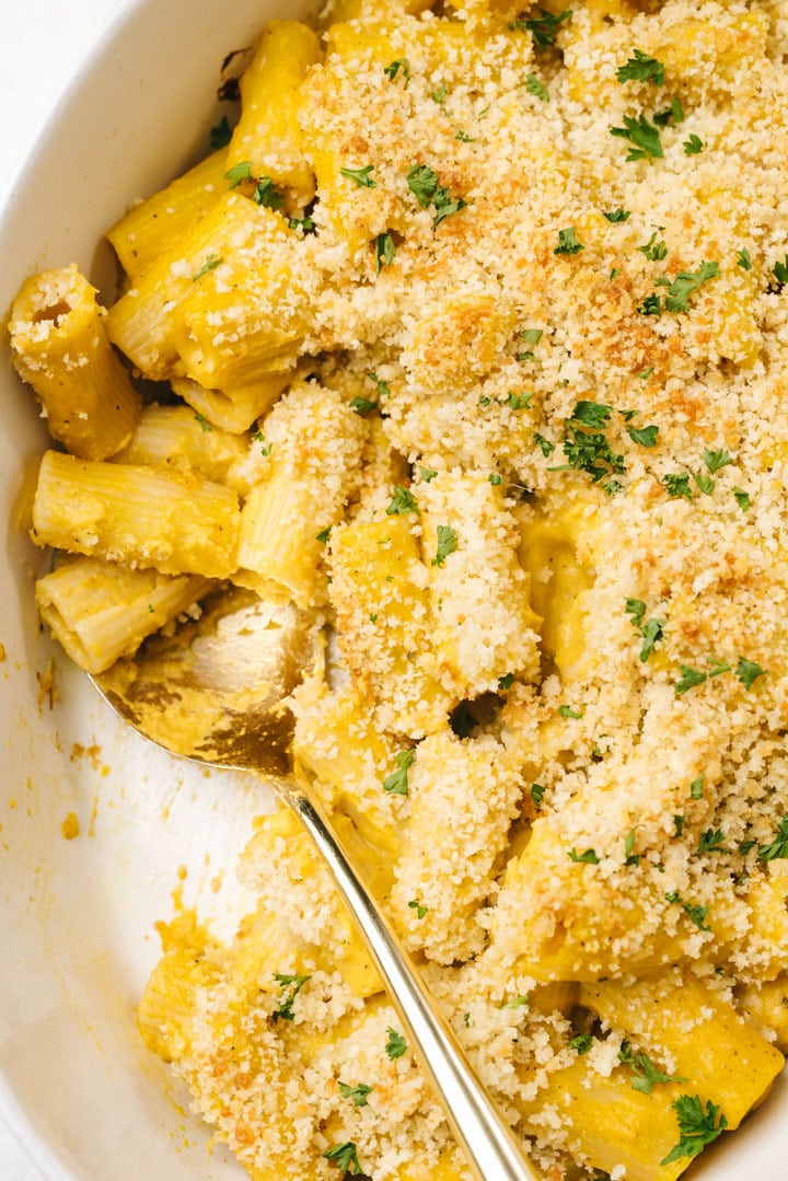 A gold serving spoon tucked into a casserole dish of baked butternut squash mac and cheese.