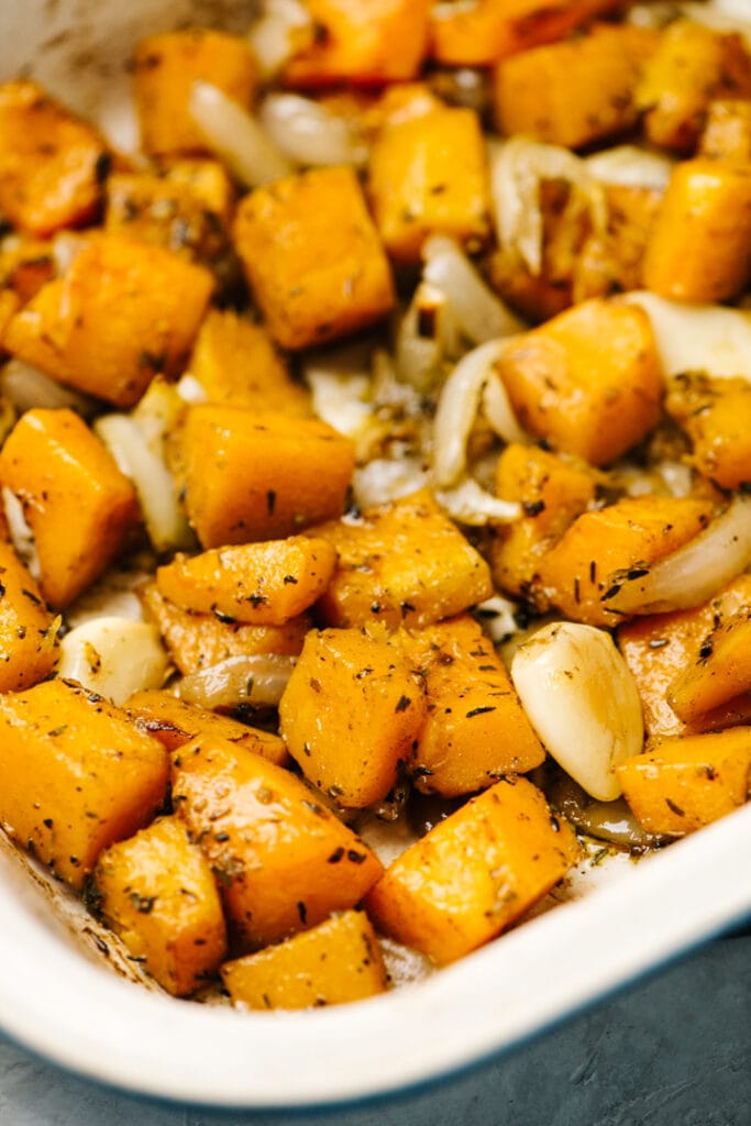 Roasted butternut squash cubes with onions and garlic cloves in a casserole dish.