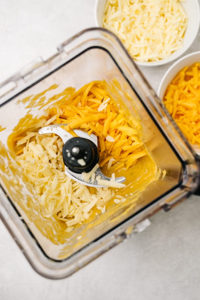Shredded cheese added to butternut squash sauce in a blender.