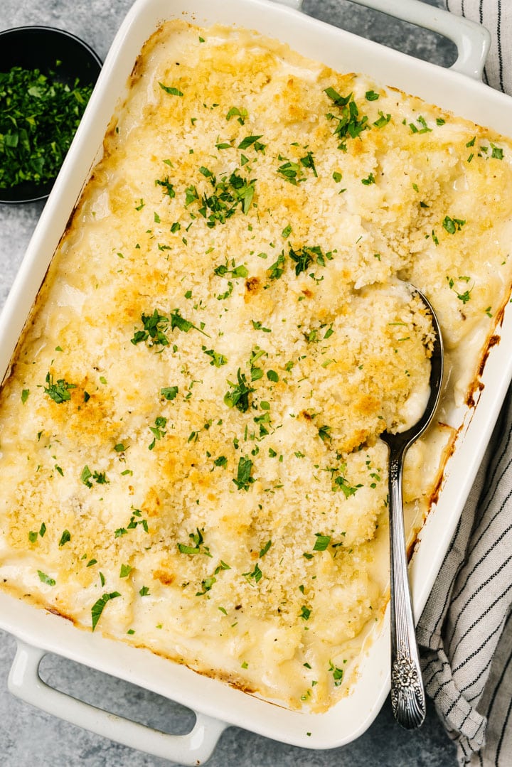 Baked cauliflower au gratin casserole garnished with parsley on a concrete background with a vintage serving spoon and striped linen napkin.