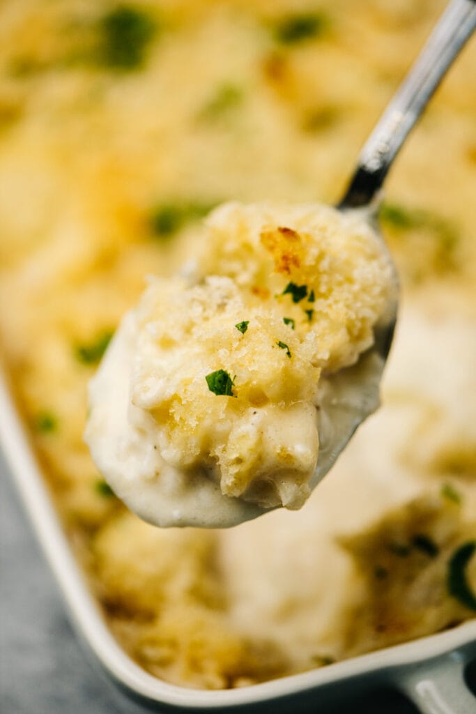 A spoonful of au gratin cauliflower hovering over a casserole dish.